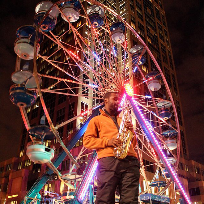 Man playing a saxophone in front of the First Night ferris wheel